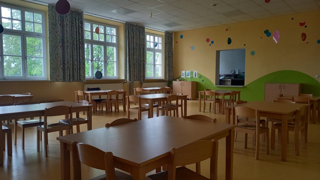Leerer Kinderzimmer mit Holztisch und -stühlen, gelbe Wände, Fenstern und Dekoration.