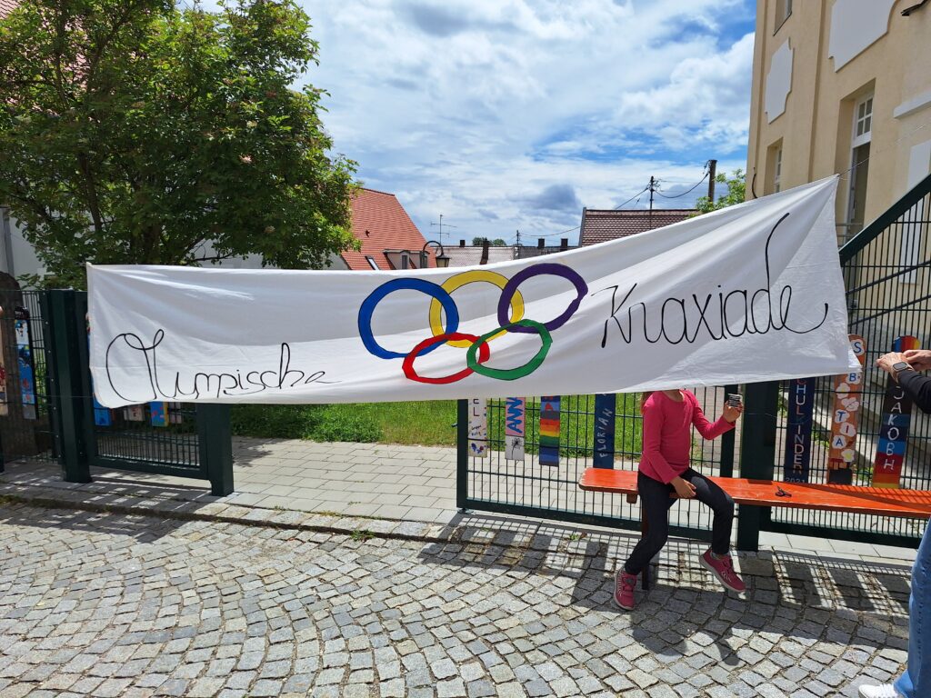 Olympische Knaxiade – Buntband mit Olympischen Ringen auf einem Wegen.