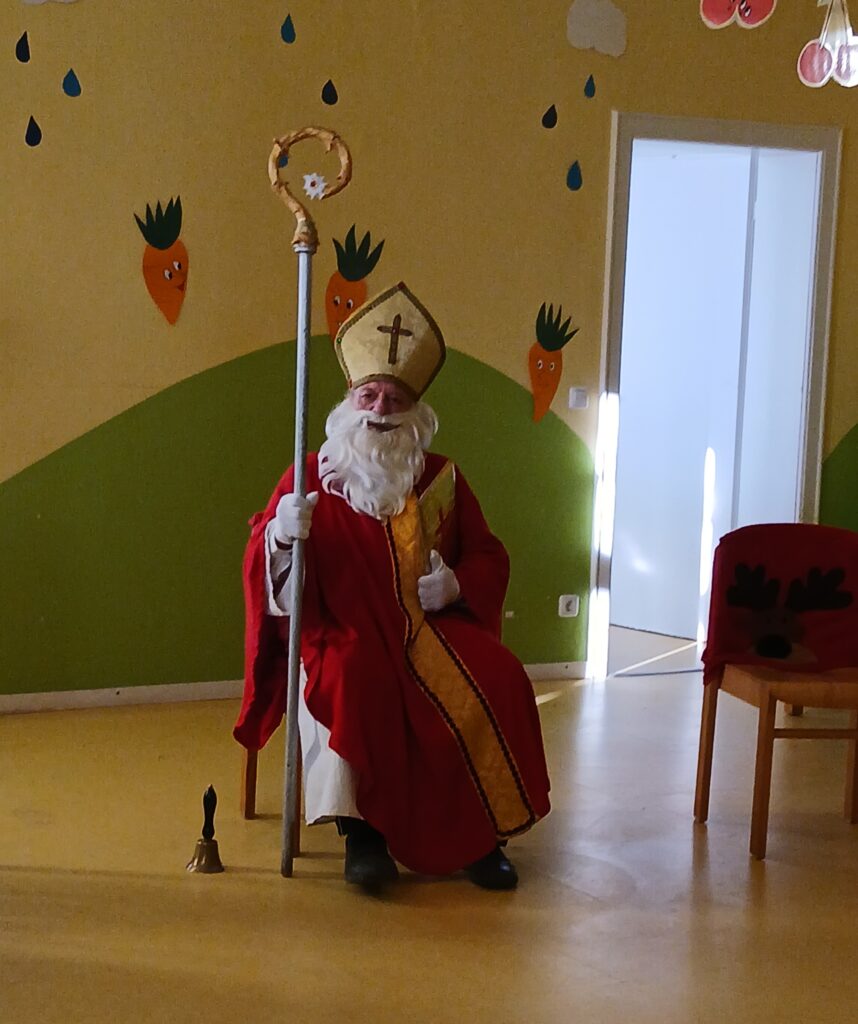 St. Nicholas in buntem Kostüm sitzt im Kinderzimmer.