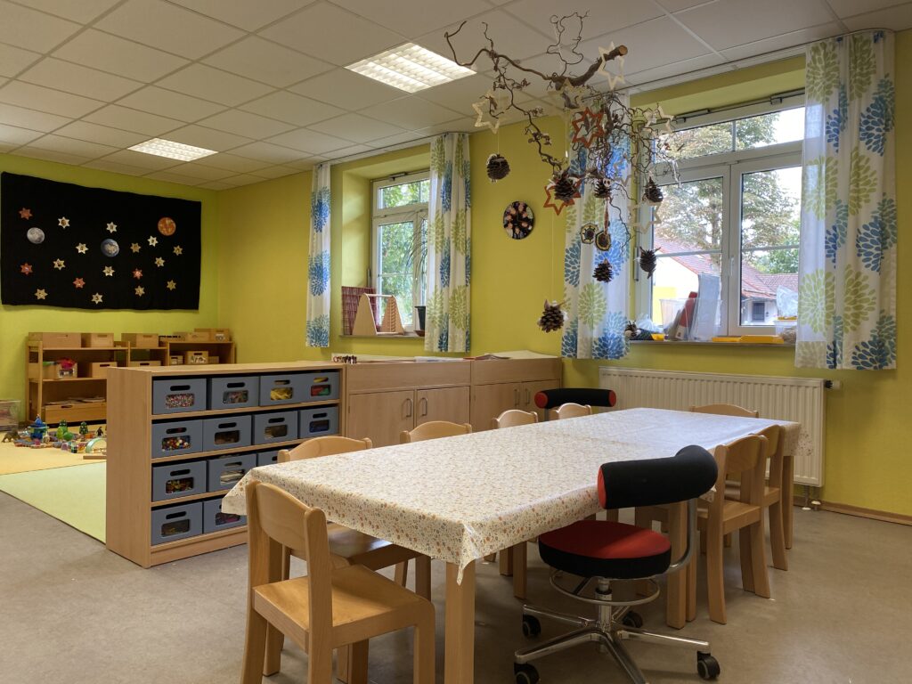 Kinderzimmer mit gelben Wänden, Tisch, Stühlen und Dekorationen.