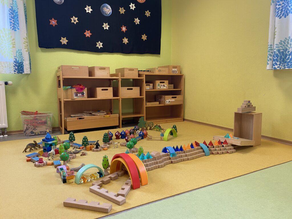 Kleinkinderkraftspielraum mit Holzbausteine, Bögen, Tieren und Spielzeug auf gelbem Teppich.