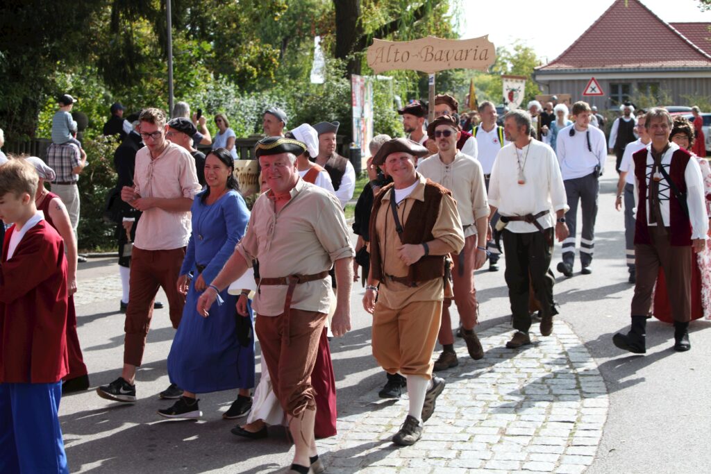 Markt Altomünster: Menschen in historischen Kostümen bei einer Parade, mit Schild "Alto-Bavaria".