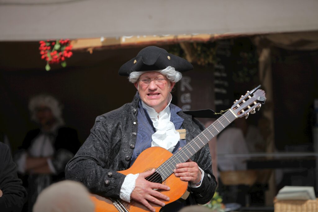 Männlicher Musiker in historischer Kleidung mit Gitarre auf Marktplatz in Altomünster.