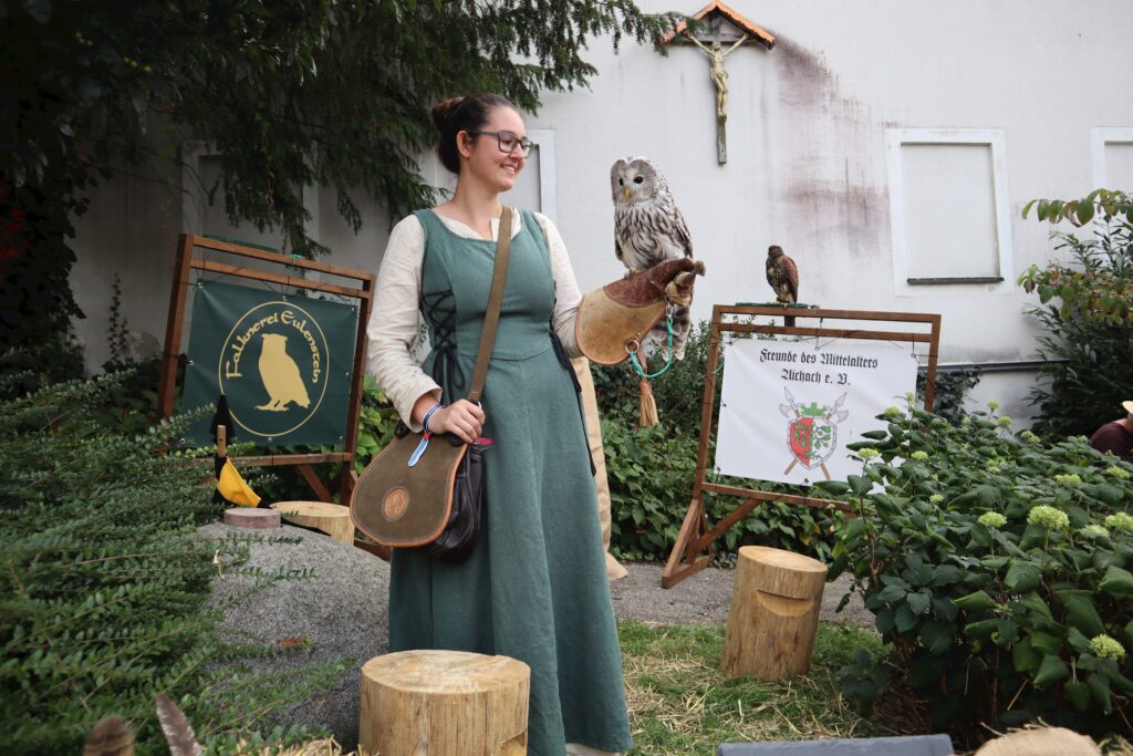 Eine Frau mit einer Eule auf dem Arm steht vor einem Markt.