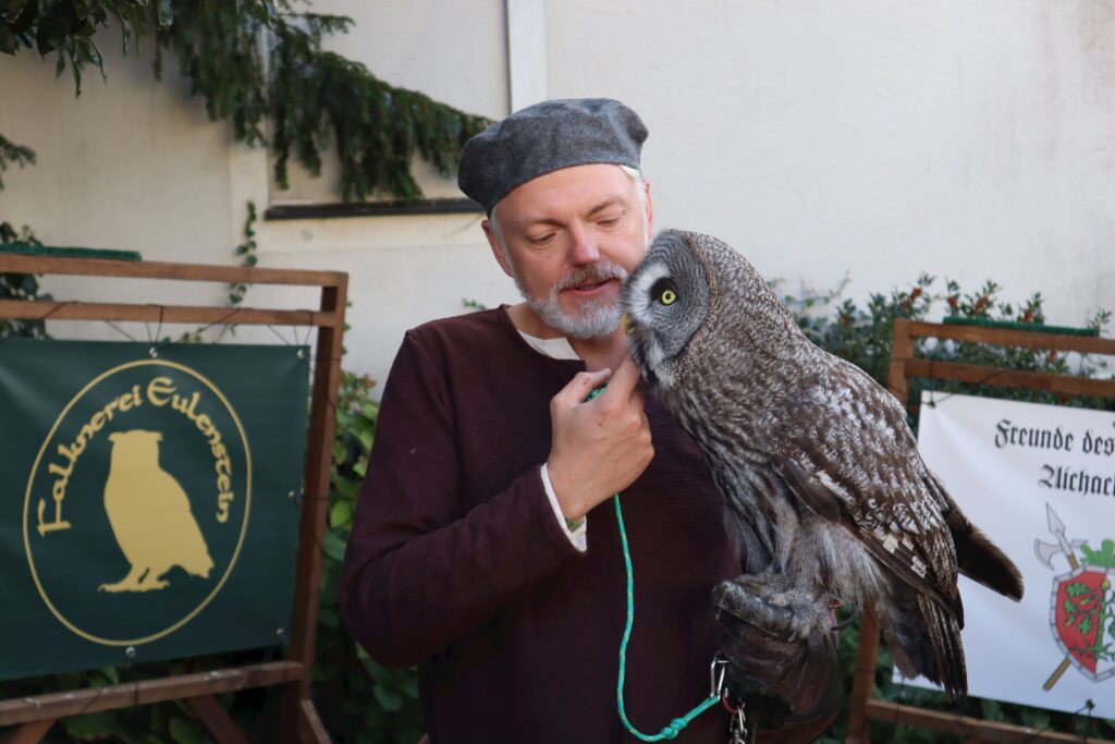 Mensch mit Eulenspiegel-Ornithologen und Graswürger am Marktplatz Altomünster.