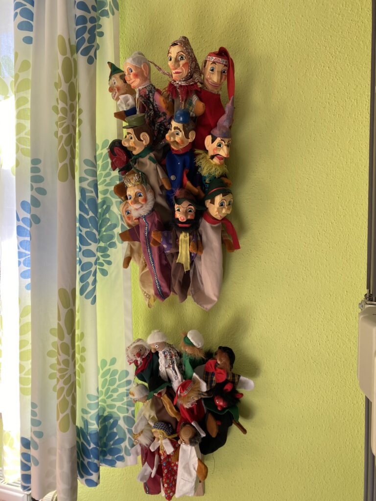 Puppen im Hintergrund einer hellen Wand mit farbenfrohen Figuren.