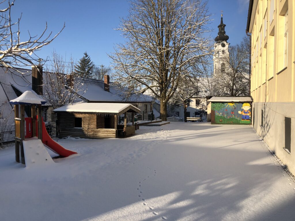 Schneekinderplatz mit Spielplatz und Kirchturm im Winter.