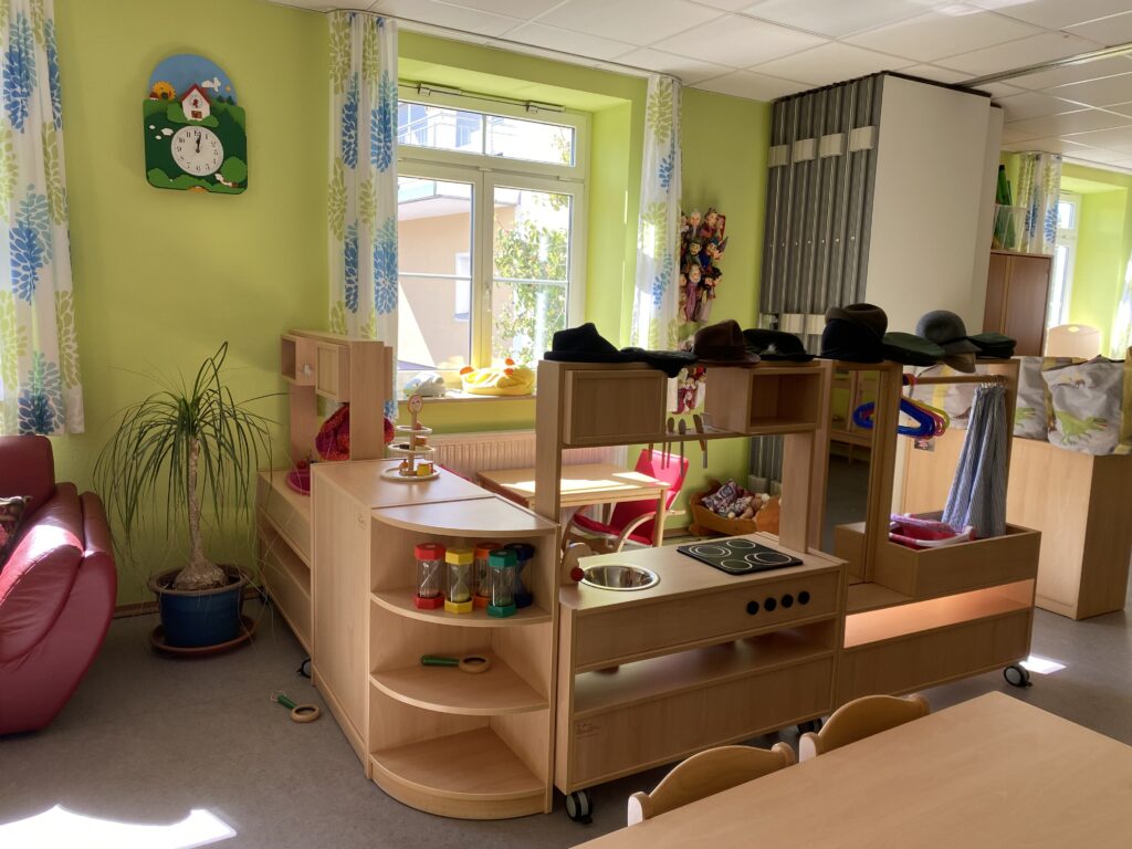 Kinderzimmer mit Spielküche, Pflanze und Wanduhr.