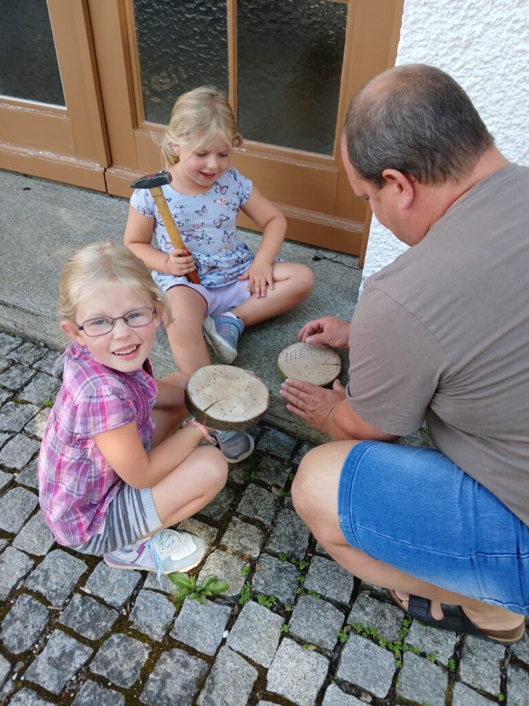 Vater und zwei Mädchen beim Holzwerk auf Pflastersteinen.