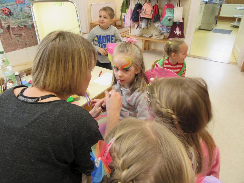 Mädchen und Lehrer an einer Wand mit bunten Gesichtsmalereien.