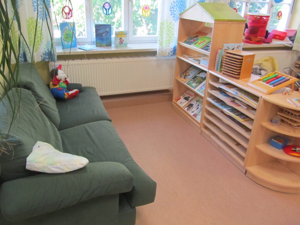 Kinderzimmer mit Sitzsängel, Bücherregal und Spielzeug.