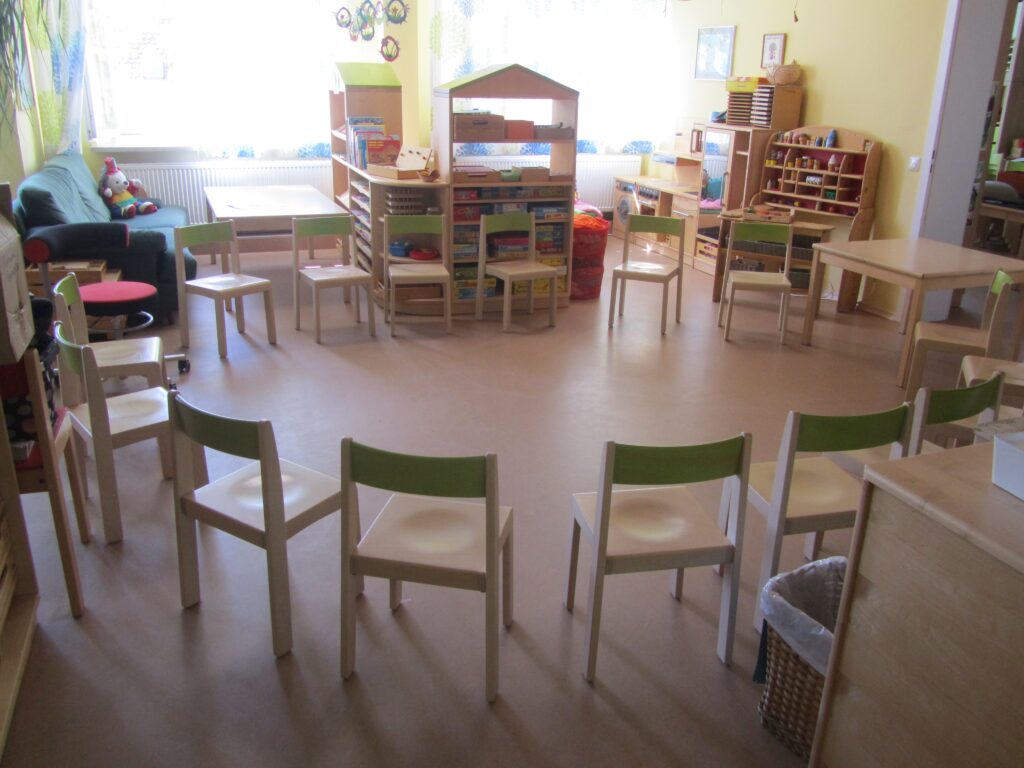 Kinderzimmer mit Tischen, Stühlen und Spielzeug im hellen Raum.