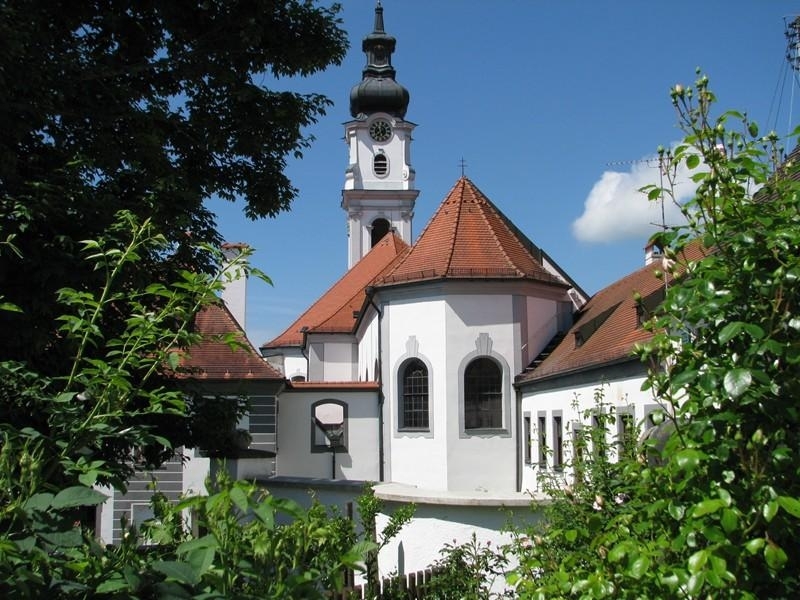Kirche Altomünster, Blick durch die Bäume auf das Gebäude mit Turm und rotem Dach.