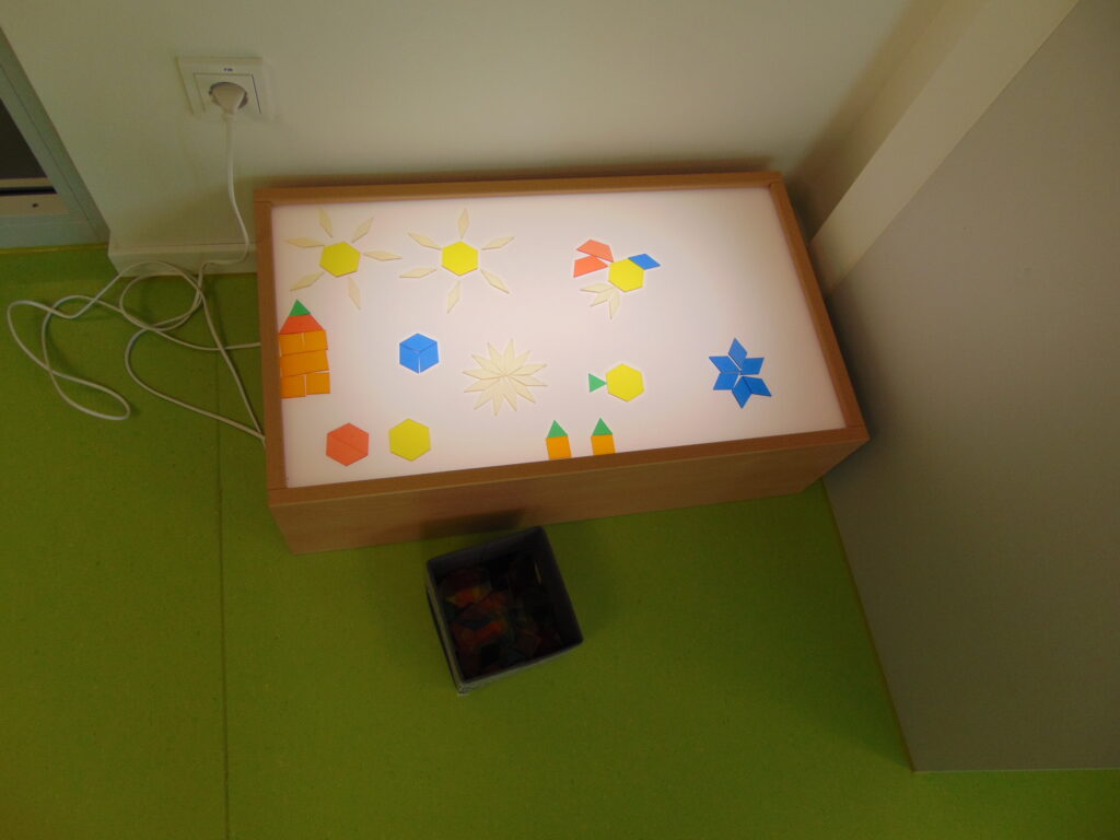 Ein beleuchteter Spielbox mit geometrischen Formen und bunten Steckern auf einer grünen Oberfläche.