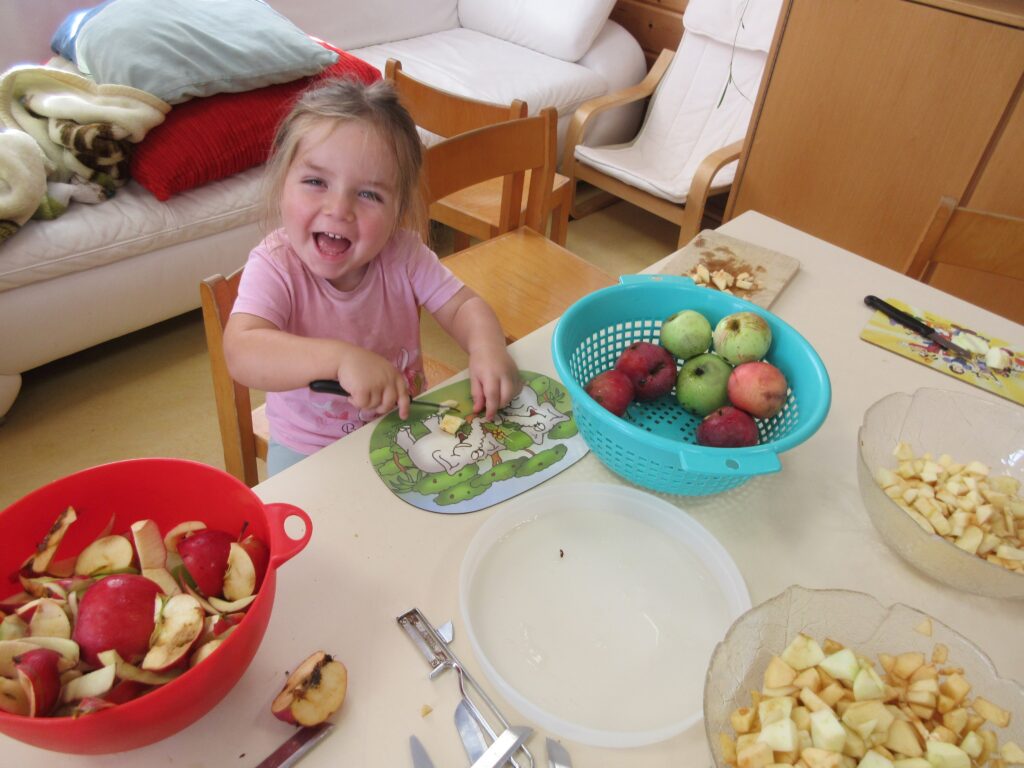 Kleines Mädchen schält Apfelschips auf Tisch.