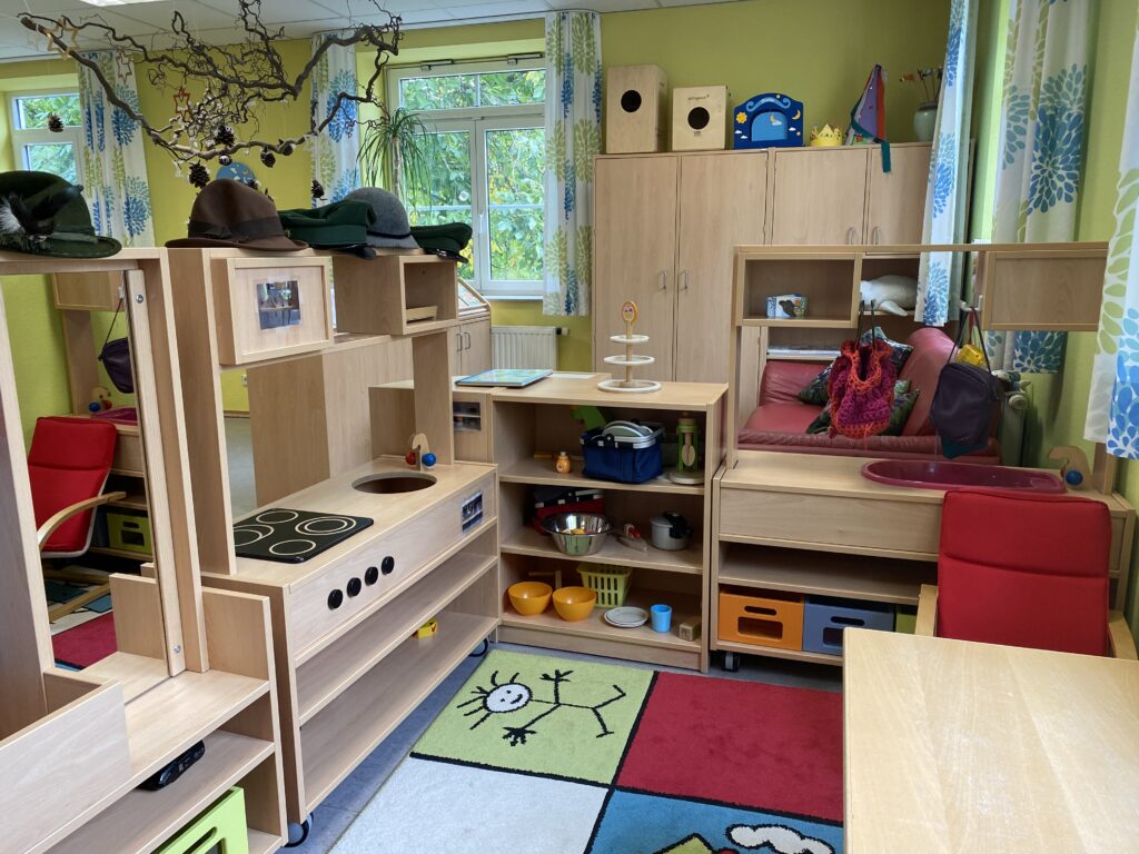 Kinderzimmer mit Spielküche, Sitzgelegenheiten und Regalbrett.