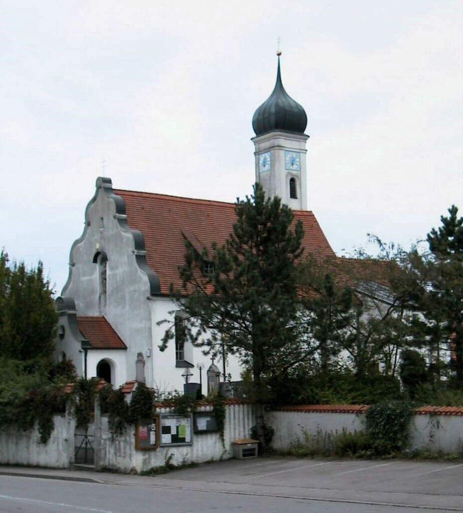 Kirche Altomünster mit Turm und rotem Dach vor einem Zaun und Bäumen.