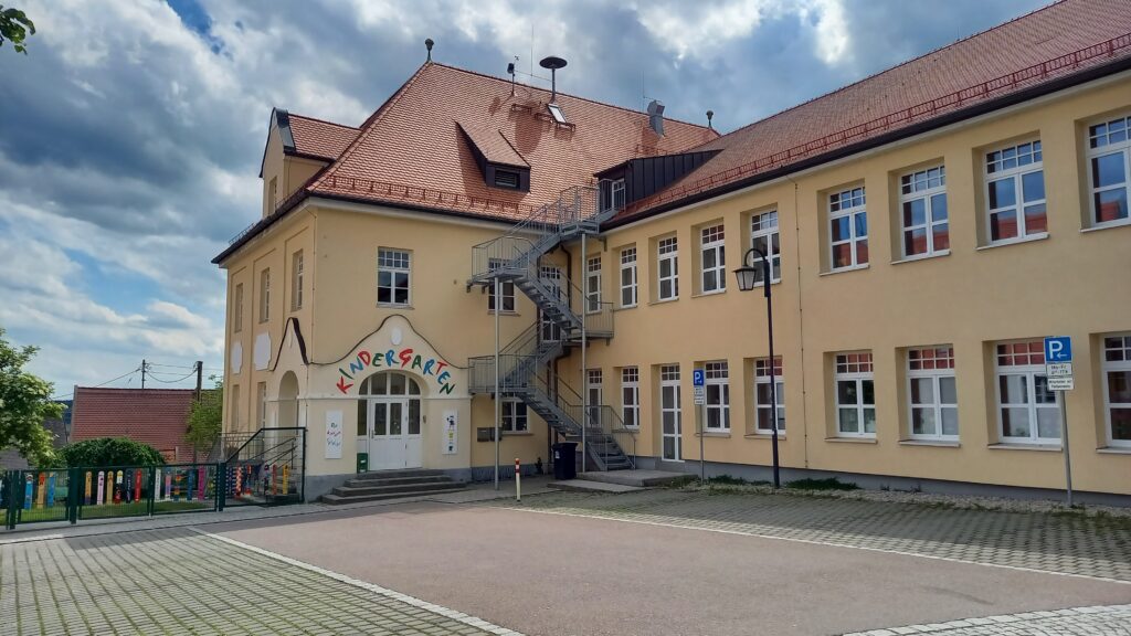 Kindergarten mit gelbem Haus und Spielzeug im Garten.