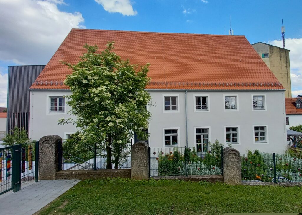 Schule mit rotem Dach und weißen Wänden vor einer Gruppe von Bäumen.