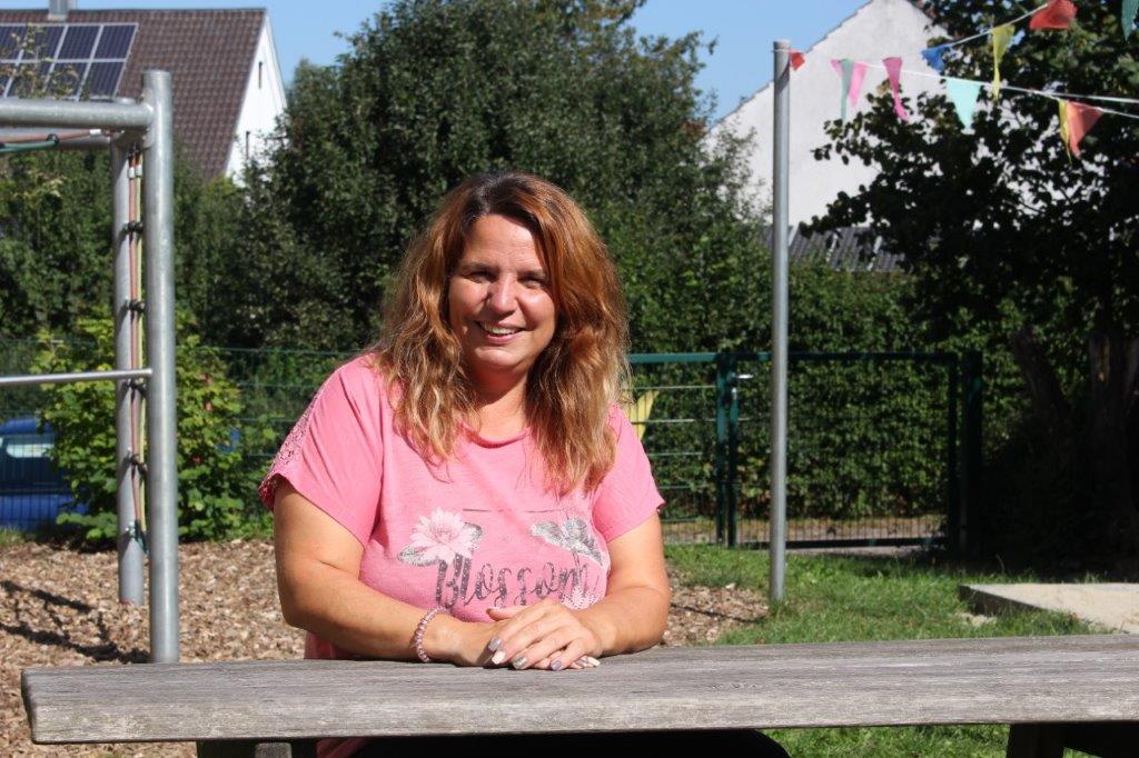Frau in rosa T-Shirt sitzt auf einer Holzbank im Garten.