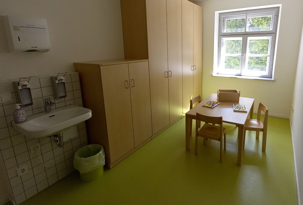 Kinderzimmer mit Tisch, Stühlen, Waschbecken und Schrank.