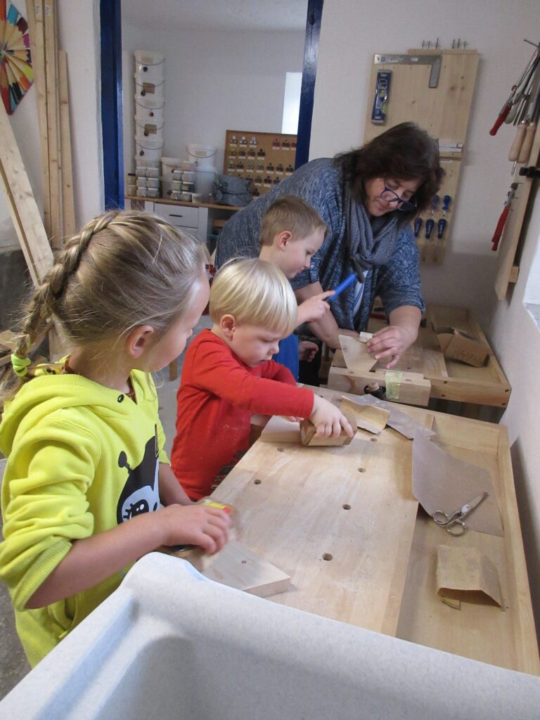 Mädchen und Erwachsene bei Holzbearbeitung in einem Werkstattumfeld.
